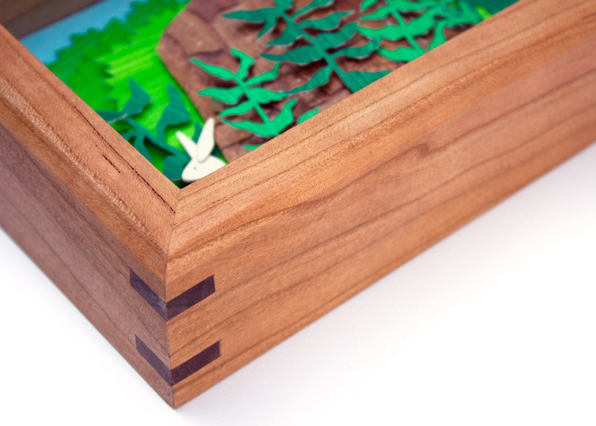 Framed cut paper illustration of bunnies around a tree stump in bushes.