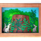 Framed cut paper illustration of bunnies around a tree stump in bushes.