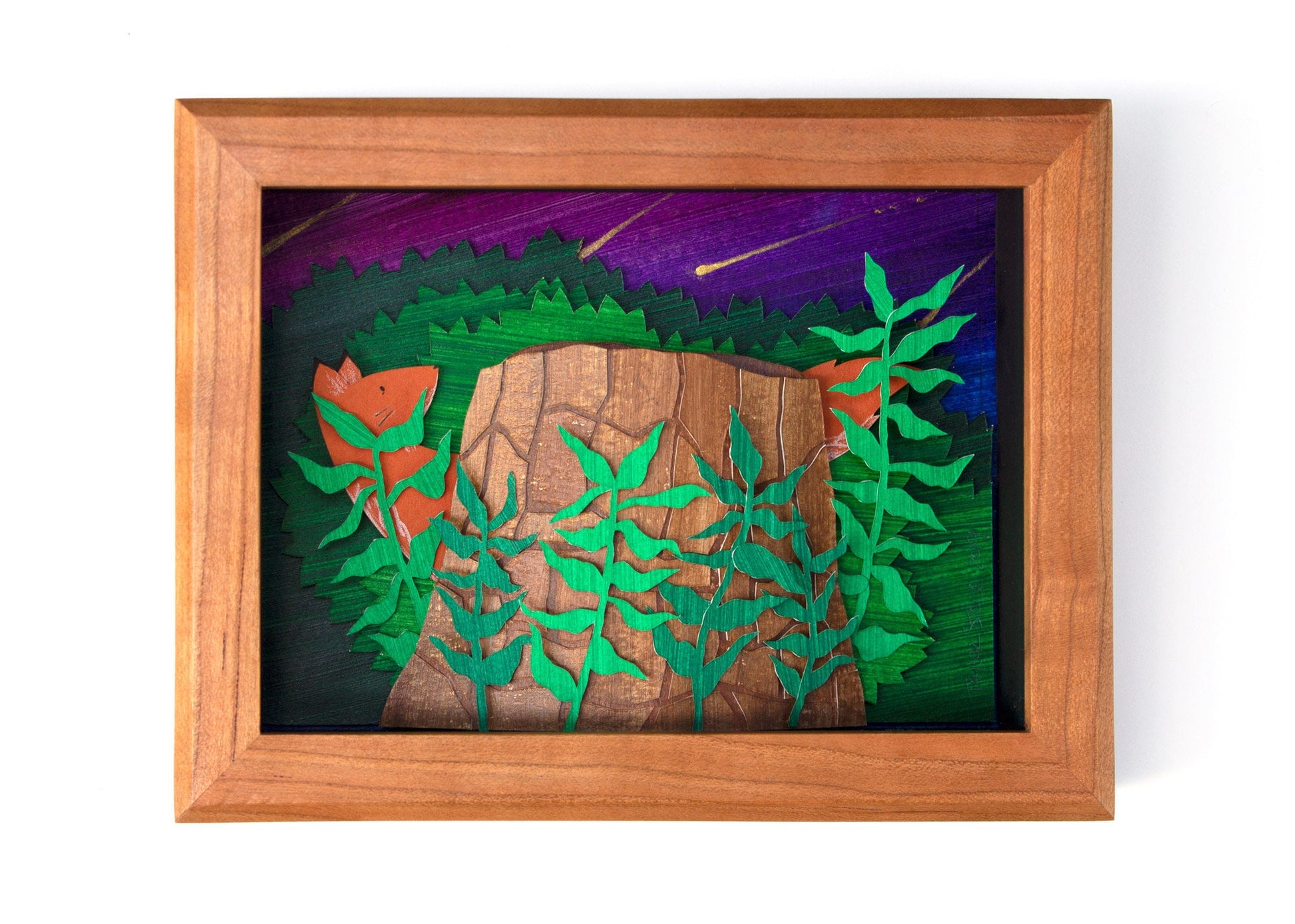 Framed cut paper illustration of fox and tree trunk with bushes at sunset