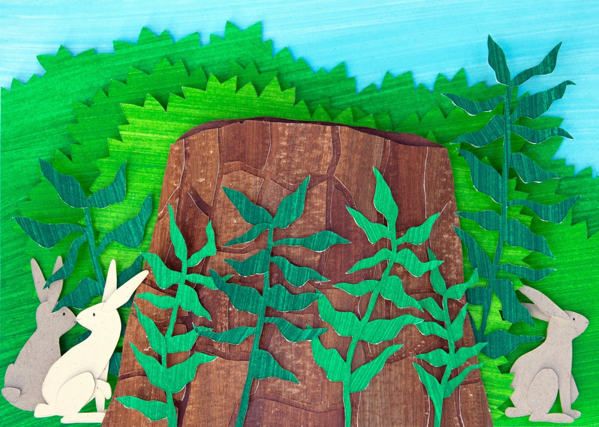 Framed cut paper illustration of bunnies around a tree stump in bushes.