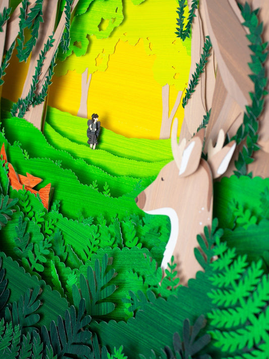 Framed cut paper illustration of cute forrest scene with deer, fox, and hiker.