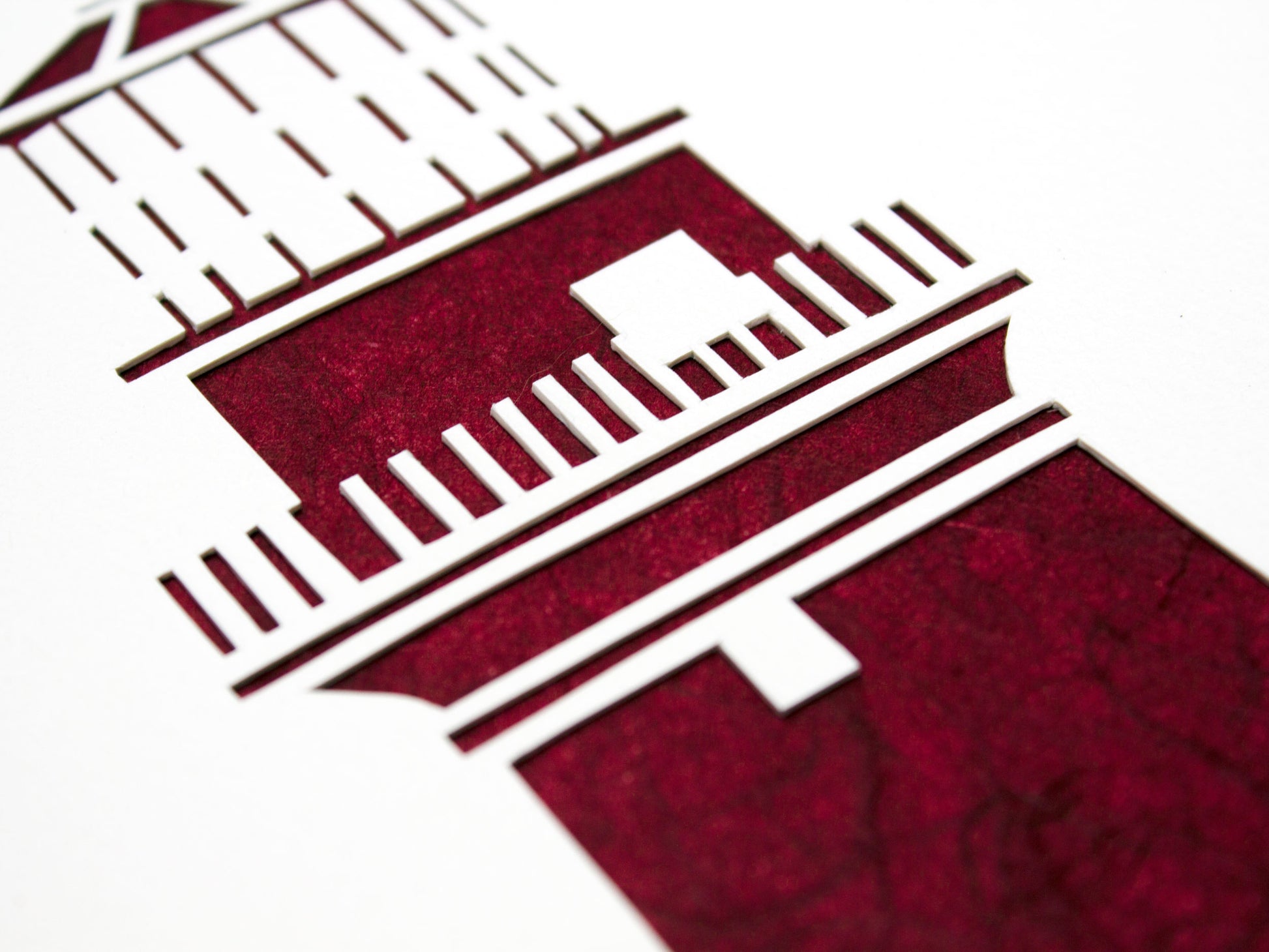 Framed simple deep red and white cut paper illustration of the Gay Head lighthouse in Aquinnah, on Martha's Vineyard.