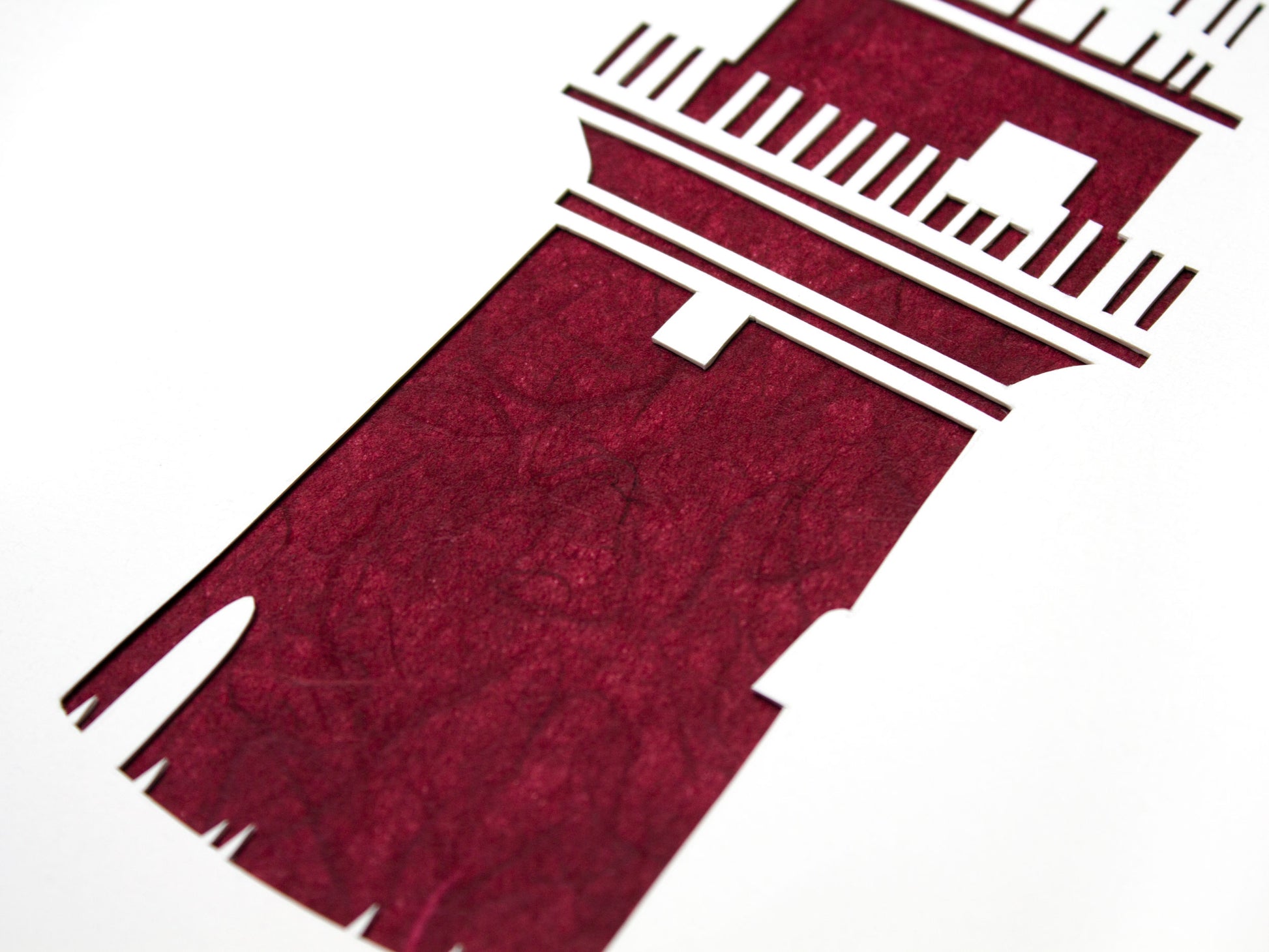 Framed simple deep red and white cut paper illustration of the Gay Head lighthouse in Aquinnah, on Martha's Vineyard.