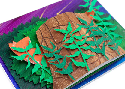 Framed cut paper illustration of fox and tree trunk with bushes at sunset