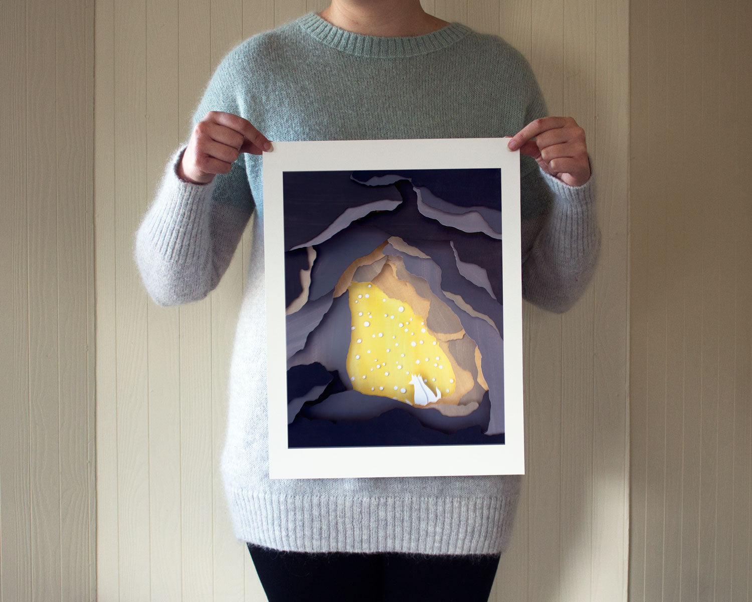 Archival print of cut paper illustration of cute scene with two foxes cuddling in a backlit snowy cave.