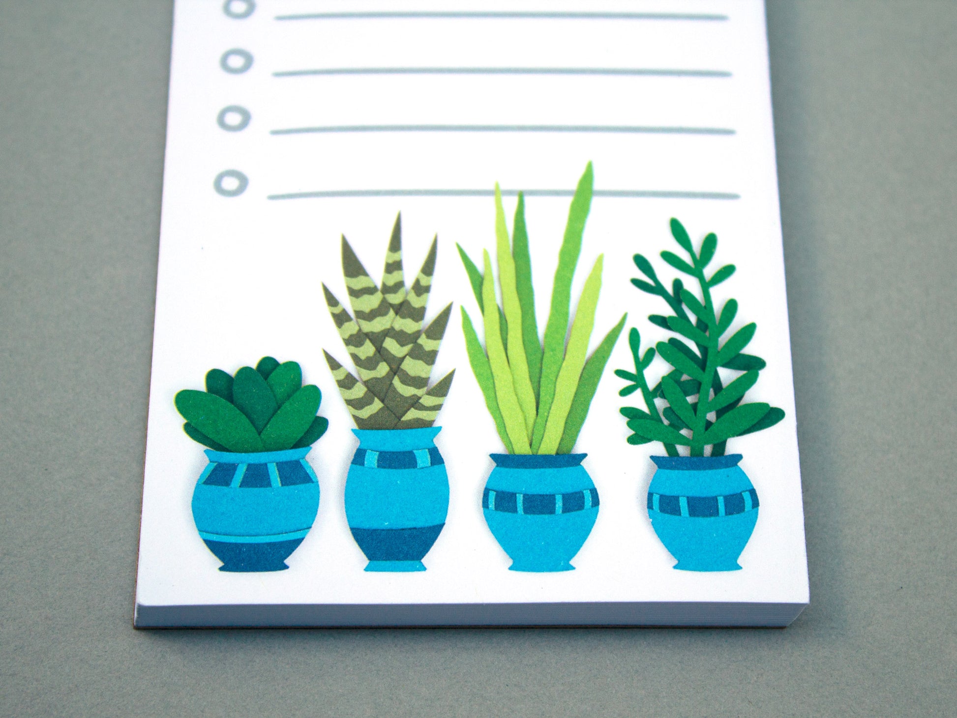Cute notepad with cut paper illustration of plants and cacti in blue pots at the bottom