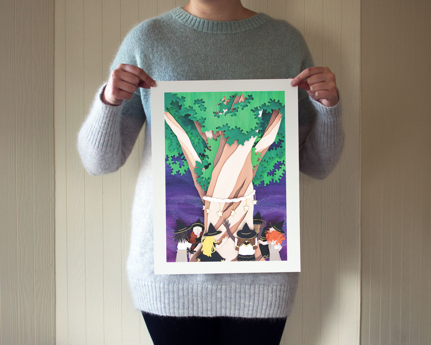 Archival print of cut paper illustration of cute whimsical scene of witches gathered around a tree at night.