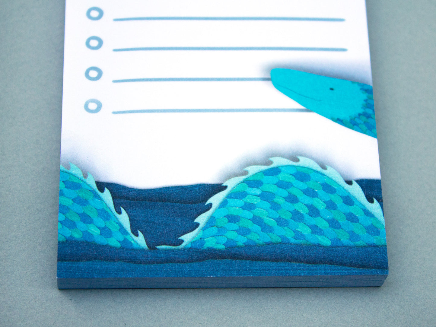 Cute notepad with cut paper illustration of blue sea serpent monster at bottom and sea gull at top.