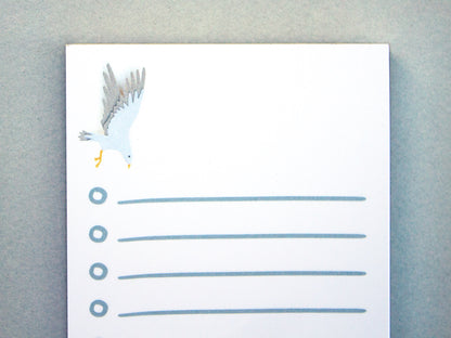 Cute notepad with cut paper illustration of blue sea serpent monster at bottom and sea gull at top.